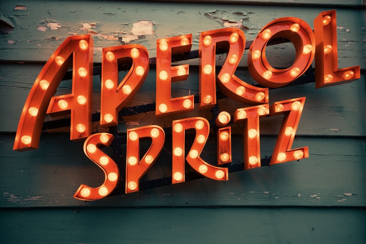 The Art of Drawing Readers In: Your attractive post title goes here Retro neon sign displaying 'Aperol Spritz' with vintage bulbs on a weathered wooden wall background.