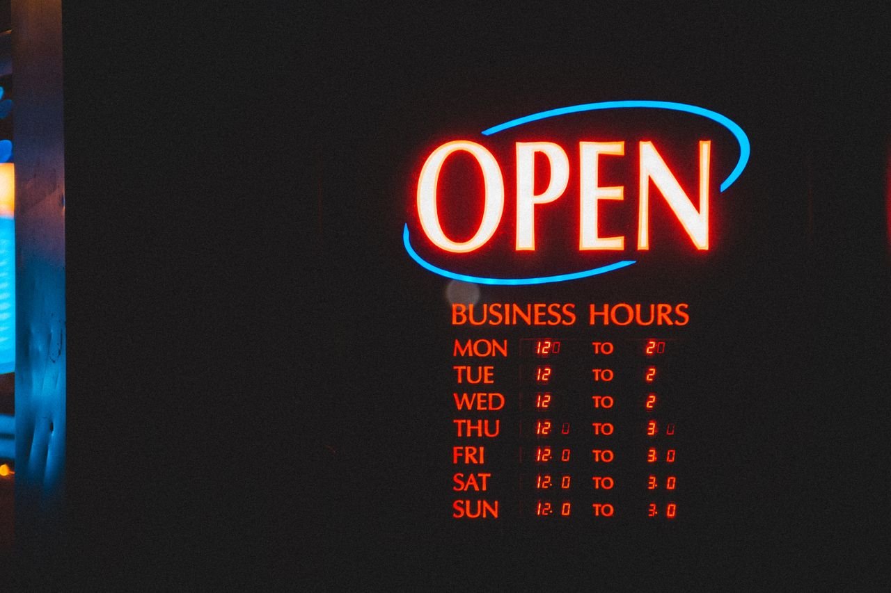 LED open sign with glowing business hours and flashing effects depicted on black board on street in city on evening time