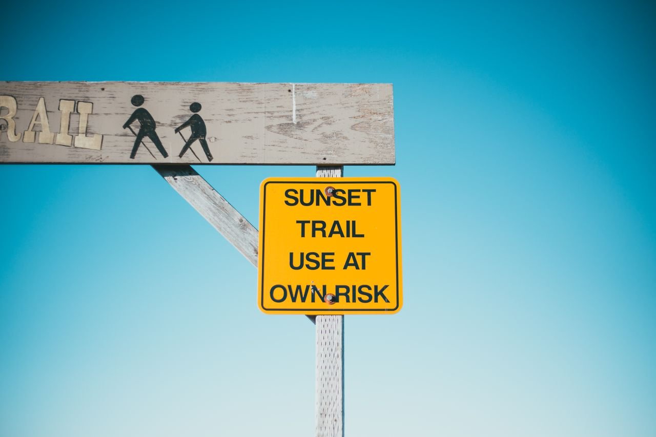 Yellow signboard with warning inscription and wooden arch on background of blue sky
