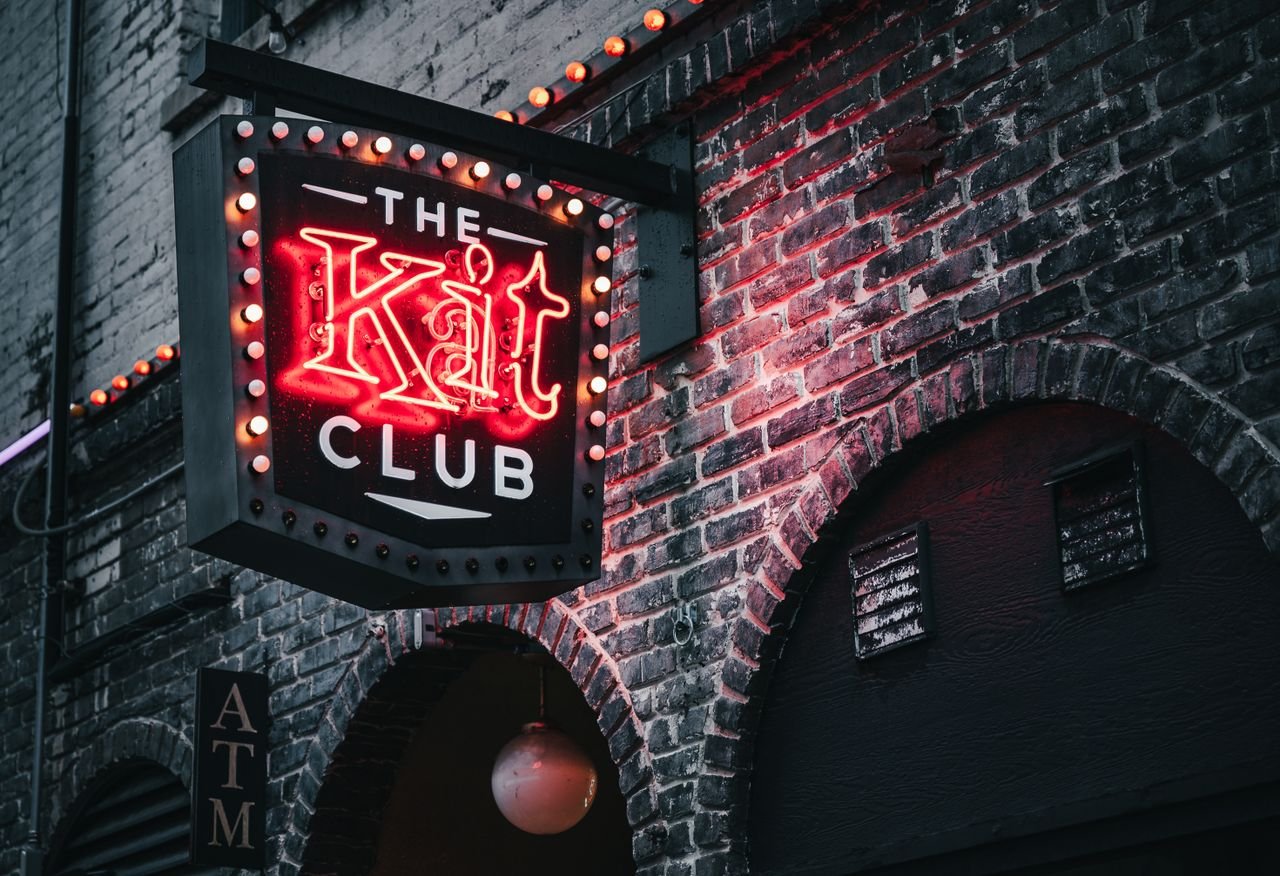 Low angle of club signboard with neon inscription hanging on old brick building in evening